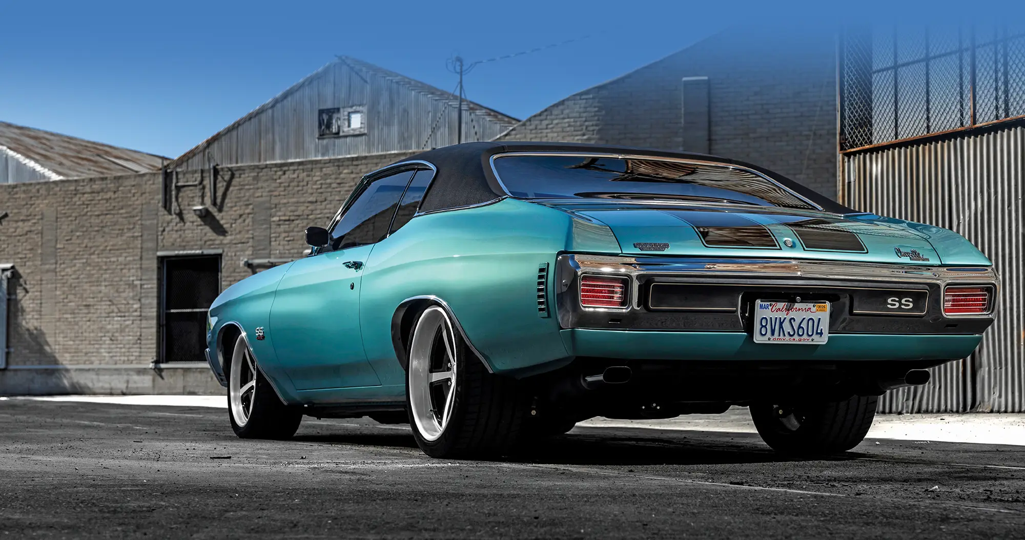 Classic teal car with a black roof parked in an industrial area.