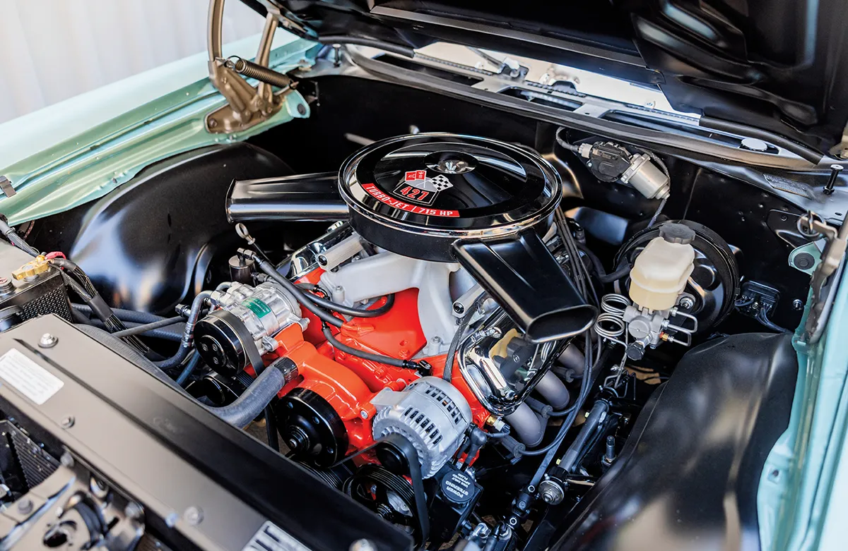 Classic car engine with a black air filter cover and orange block under an open hood.