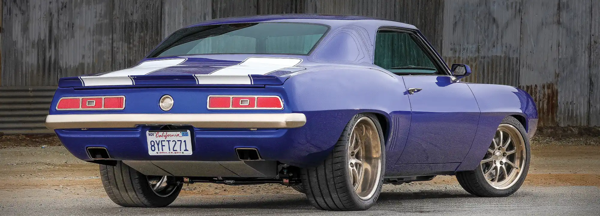 1969 Chevy Camaro rear angle, blue paint, white stripes, and modern performance wheels