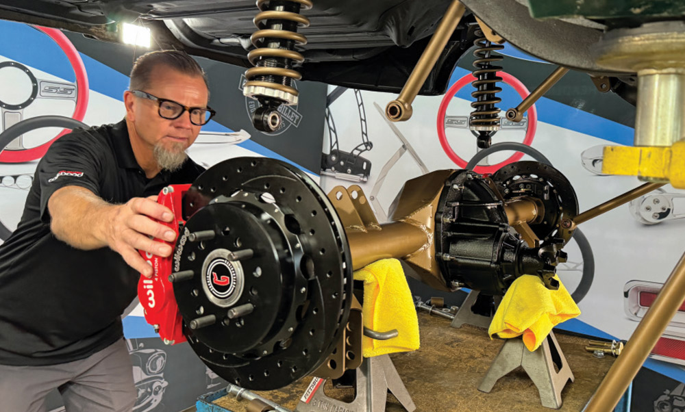 installing the rear Wilwood caliper onto the brake rotor of the 1972 Chevrolet Nova under a lifted suspension setup