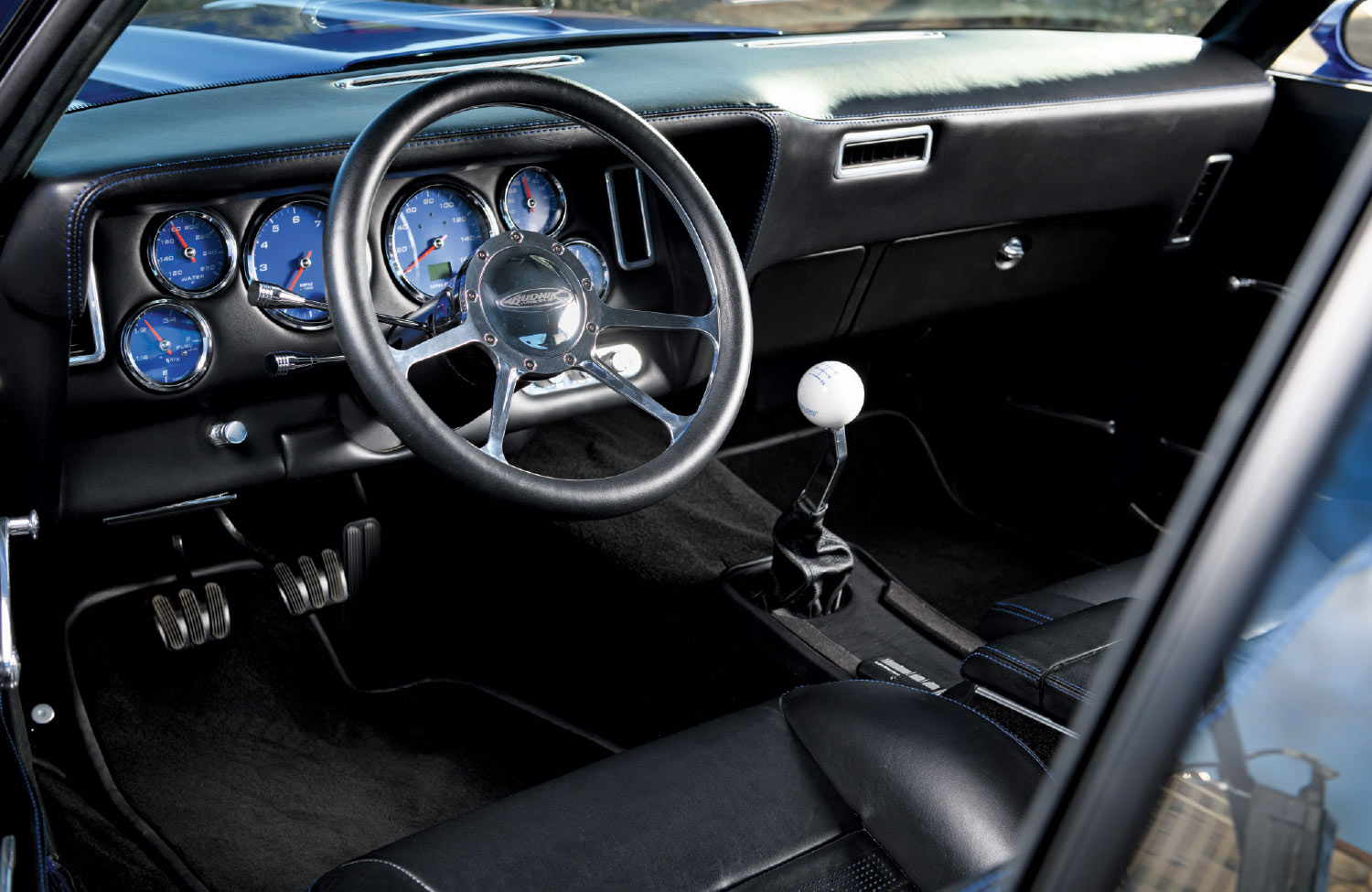 1969 Chevrolet Camaro interior with modern gauges, custom steering wheel, and a classic white Hurst shifter