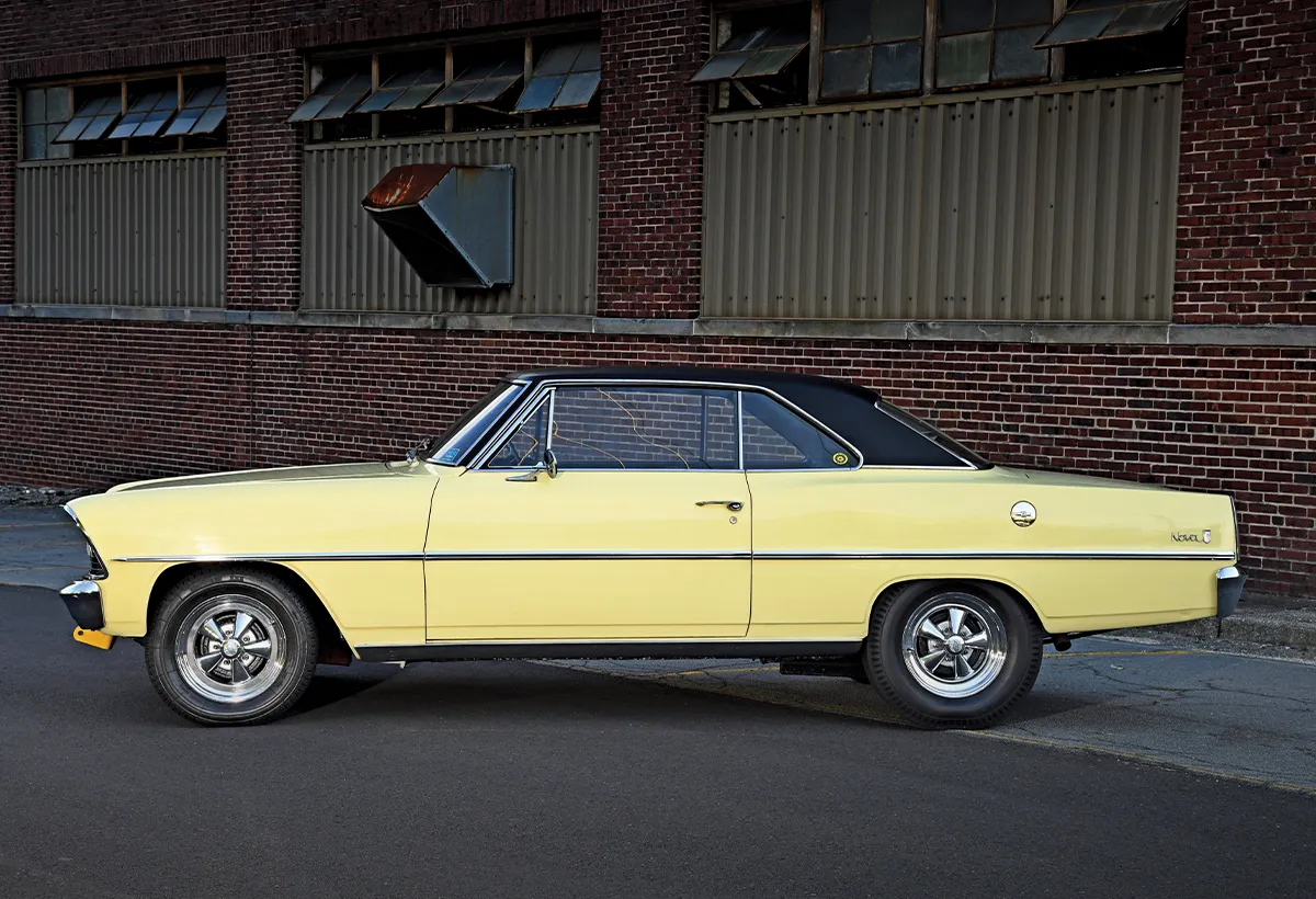 1967 Chevrolet Nova SS in yellow with black vinyl top, chrome Cragar wheels, parked by industrial brick walls