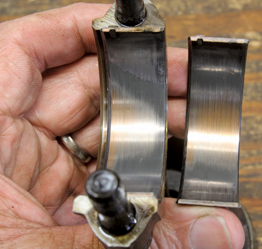 Hand holding two engine bearings with visible wear marks and smooth polished surfaces