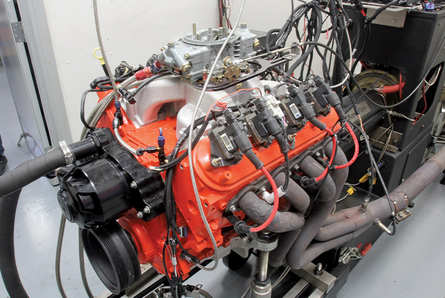 High-performance V8 engine with orange block and carburetor setup undergoing dynamometer testing with connected wiring
