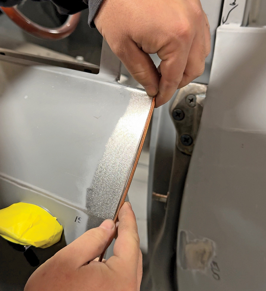 technician positioning a thin copper strip between door edges for gap uniformity