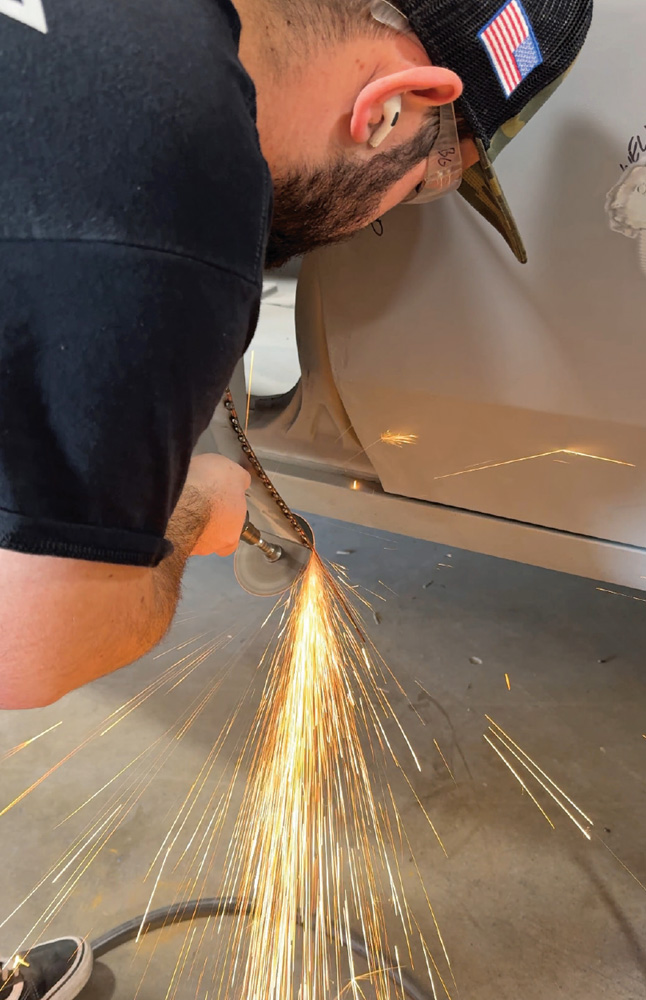 technician grinding weld seams on the lower door panel, sparks flying