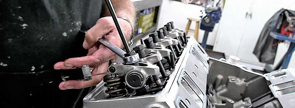 Technician fine-tuning rocker arm clearances on a fully assembled cylinder head
