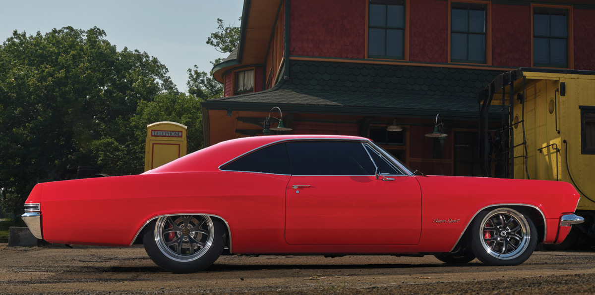 1965 Chevrolet Impala SS, red, side profile view, lowered stance, custom wheels, against vintage train station background