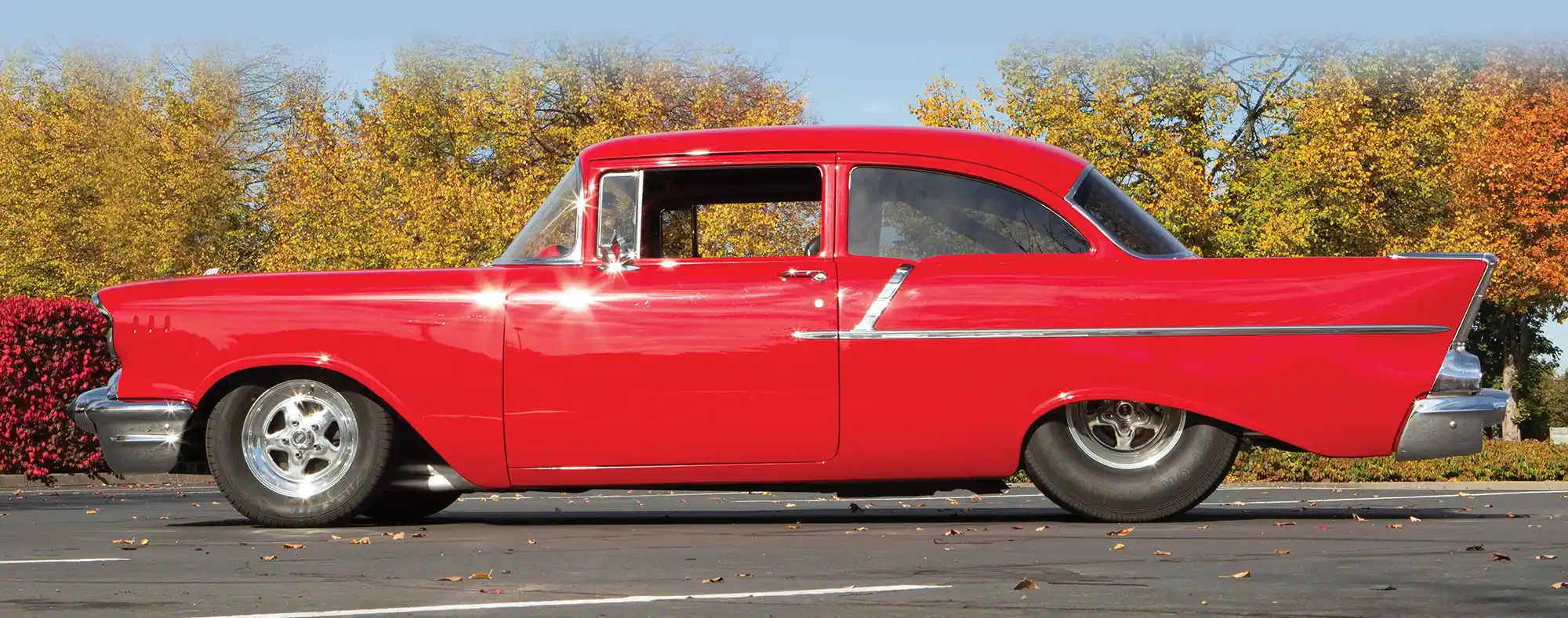 1957 Chevrolet Bel Air side profile showcasing bright red paint, classic fins, and a lowered hot rod stance