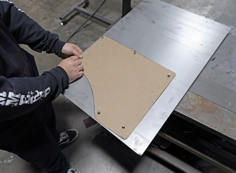 cardboard template is placed on a sheet of metal, ready to be traced and cut for the replacement panel