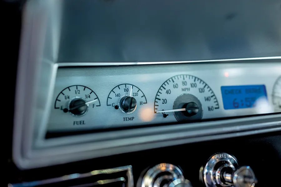 Close-up of modern aftermarket gauges (fuel, temperature, speedometer) installed in the dashboard of a classic car, with a digital clock displaying 6:55.