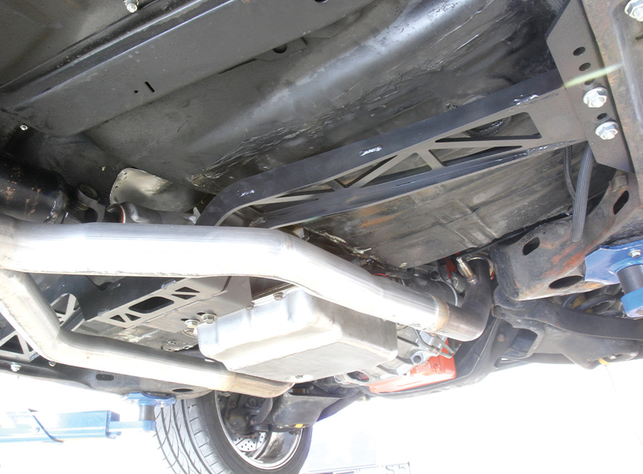 Underside view of a car showing custom exhaust pipes, oil pan, and subframe, highlighting automotive modifications and engineering.