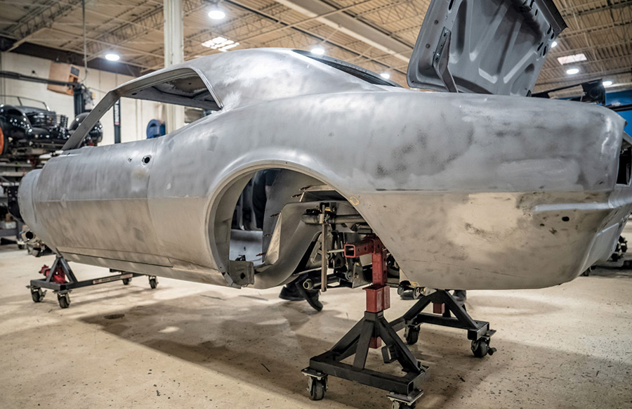 Classic car body stripped to bare metal, mounted on stands in a workshop, ready for extensive custom modifications and paintwork.