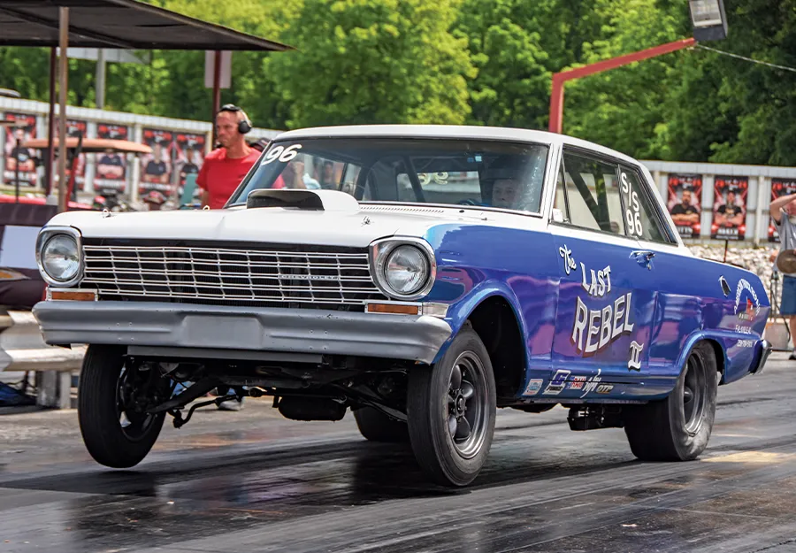 Vintage Chevrolet Nova drag car, car number '96', with a large hood scoop and custom paint, at a motorsports event.