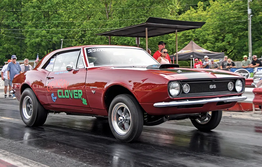 Vintage muscle car with 'Crimson Clover' painted on its side, at the starting line of an outdoor drag racing event.