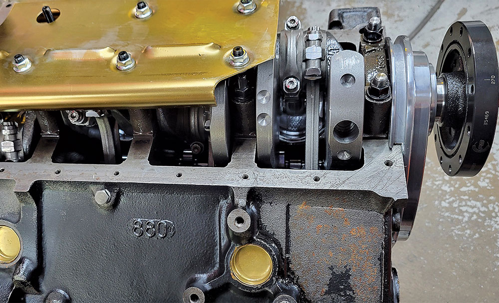 A close-up view of the front of a partially assembled engine block, showing the crankshaft, connecting rods, and the front main cap area.