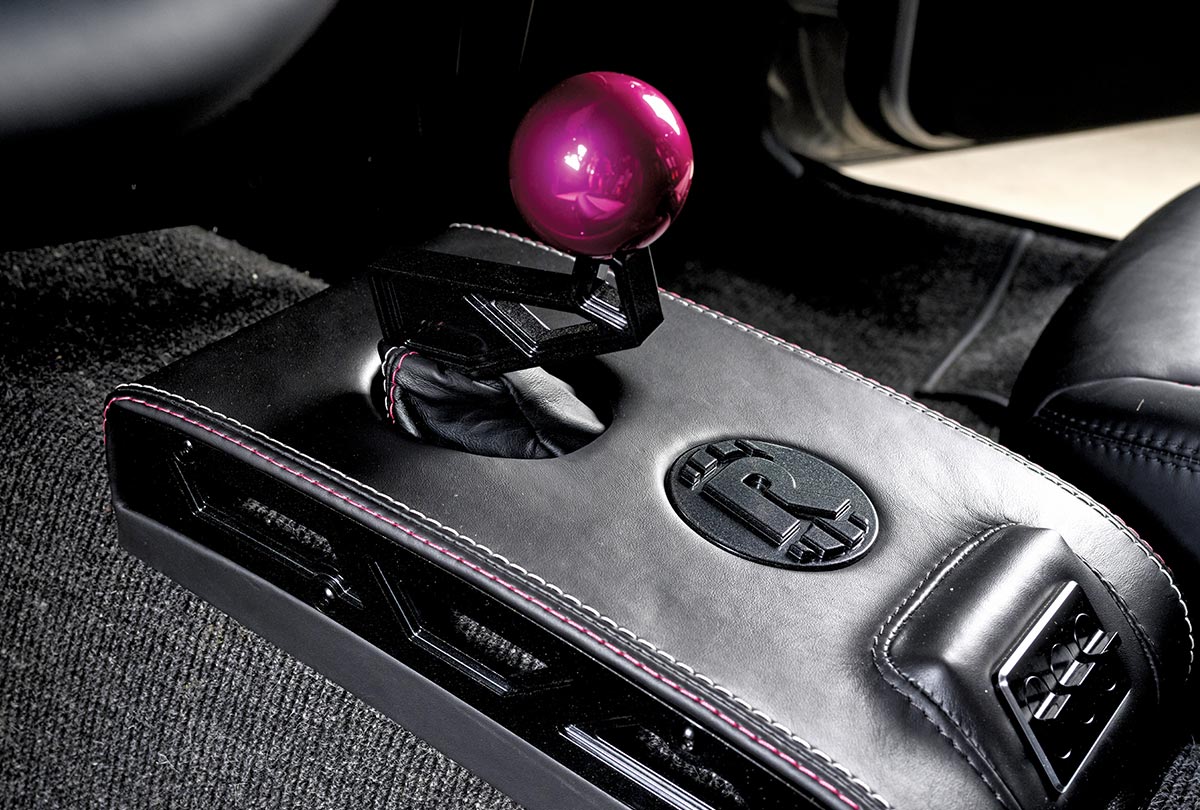 close-up view of a limited-edition 1969 Nova's black leather shifter console with pink stitching, featuring a prominent pink spherical shift knob