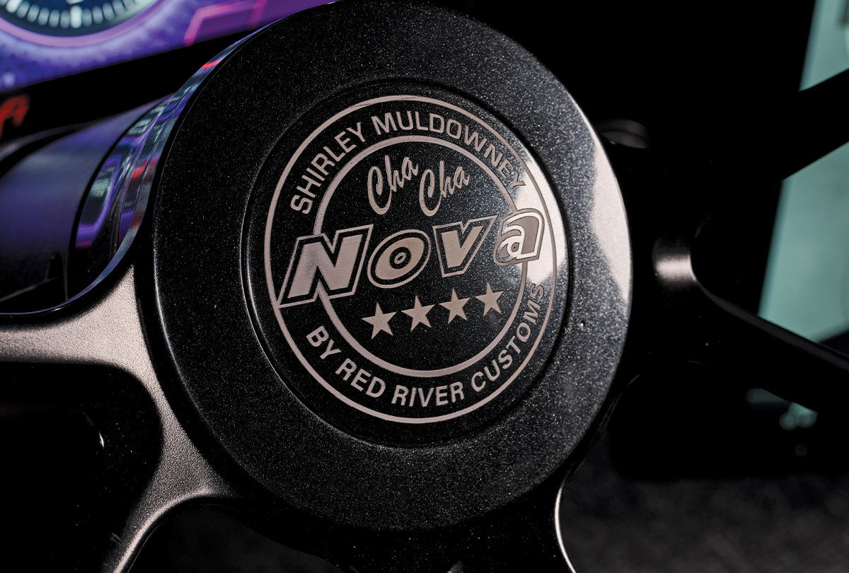 a close-up of a limited-edition 1969 Nova's steering wheel horn button with "Shirley Muldowney Cha Cha Nova by Red River Customs" and five stars inscribed on it