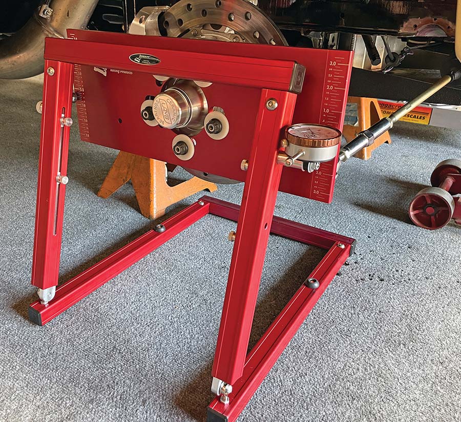 A large, bright red bump steer gauge tool set up in a garage with a dial indicator on the right side and a vertical ruler