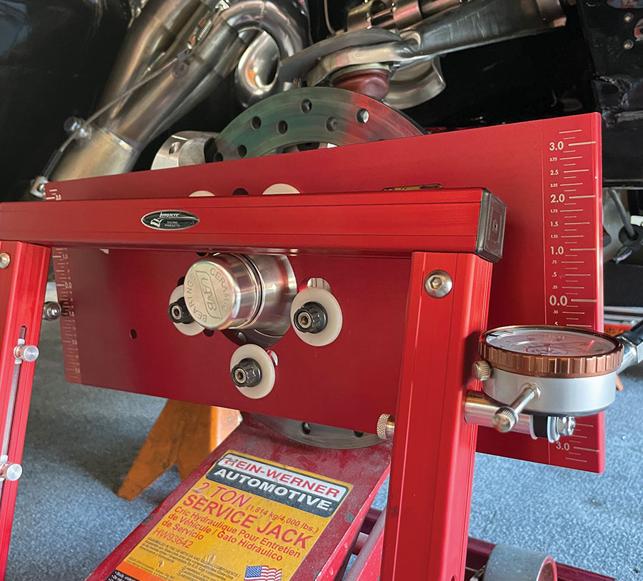 close-up of a red automotive bump steer gauge tool mounted to the front wheel hub of a race car