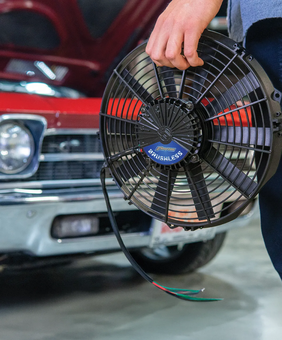 Proform 16-inch brushless electric fan hand-held next to classic red 1969 Chevrolet