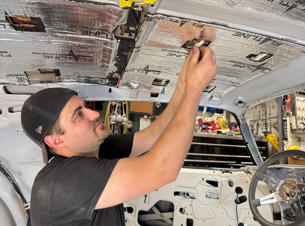 A person secures sound-deadening material to the interior roof of a restored car before the new headliner is installed.