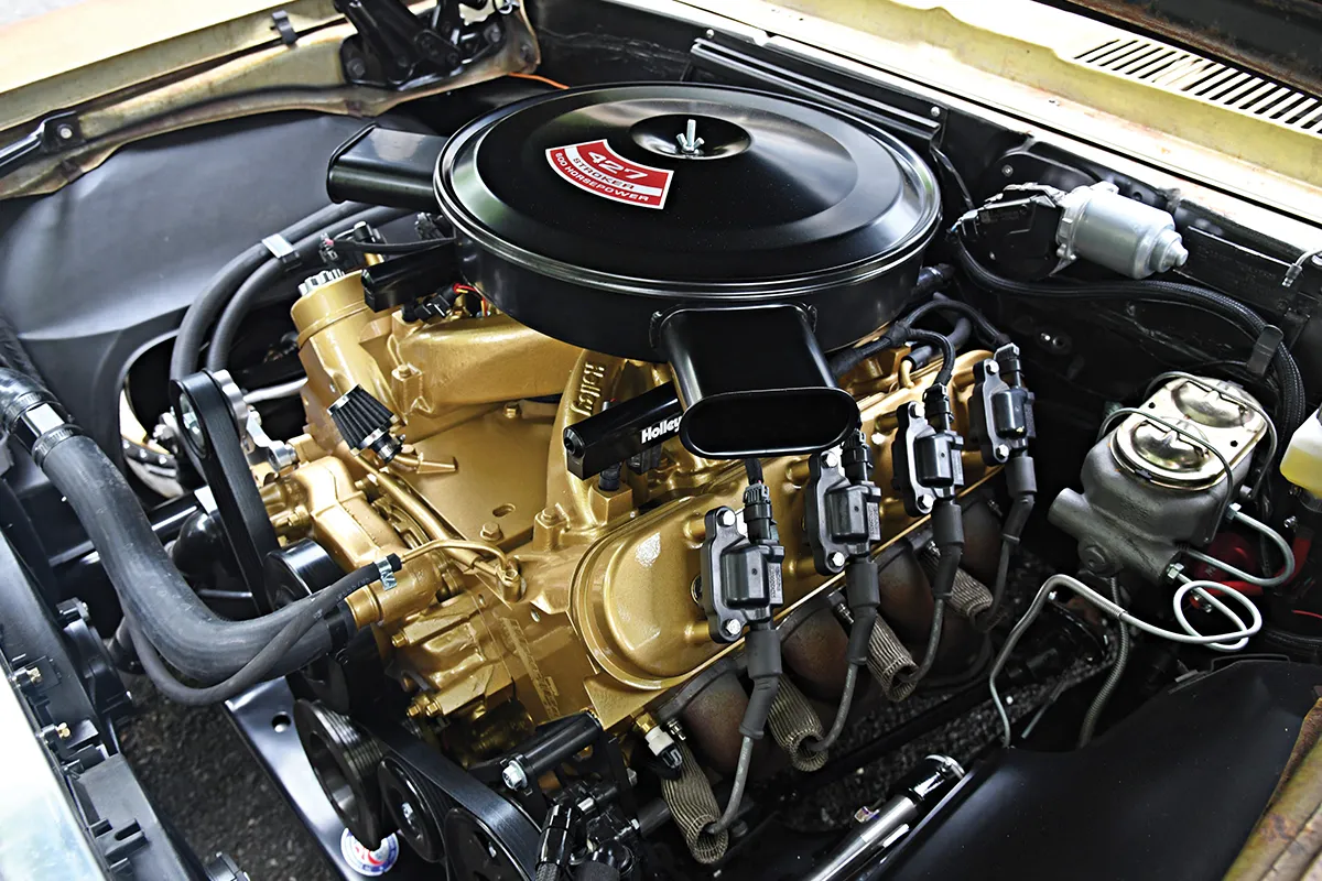 Customized big-block V8 engine painted gold with modern fuel injection, coil-on-plug ignition, and a 427 air cleaner in a classic car engine bay.