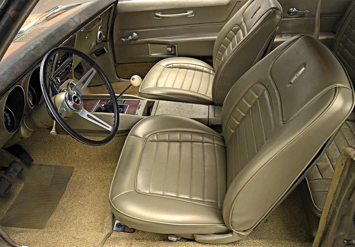 Restored classic Camaro interior featuring tan or olive gold bucket seats, matching carpet, and a center console with a manual shifter.