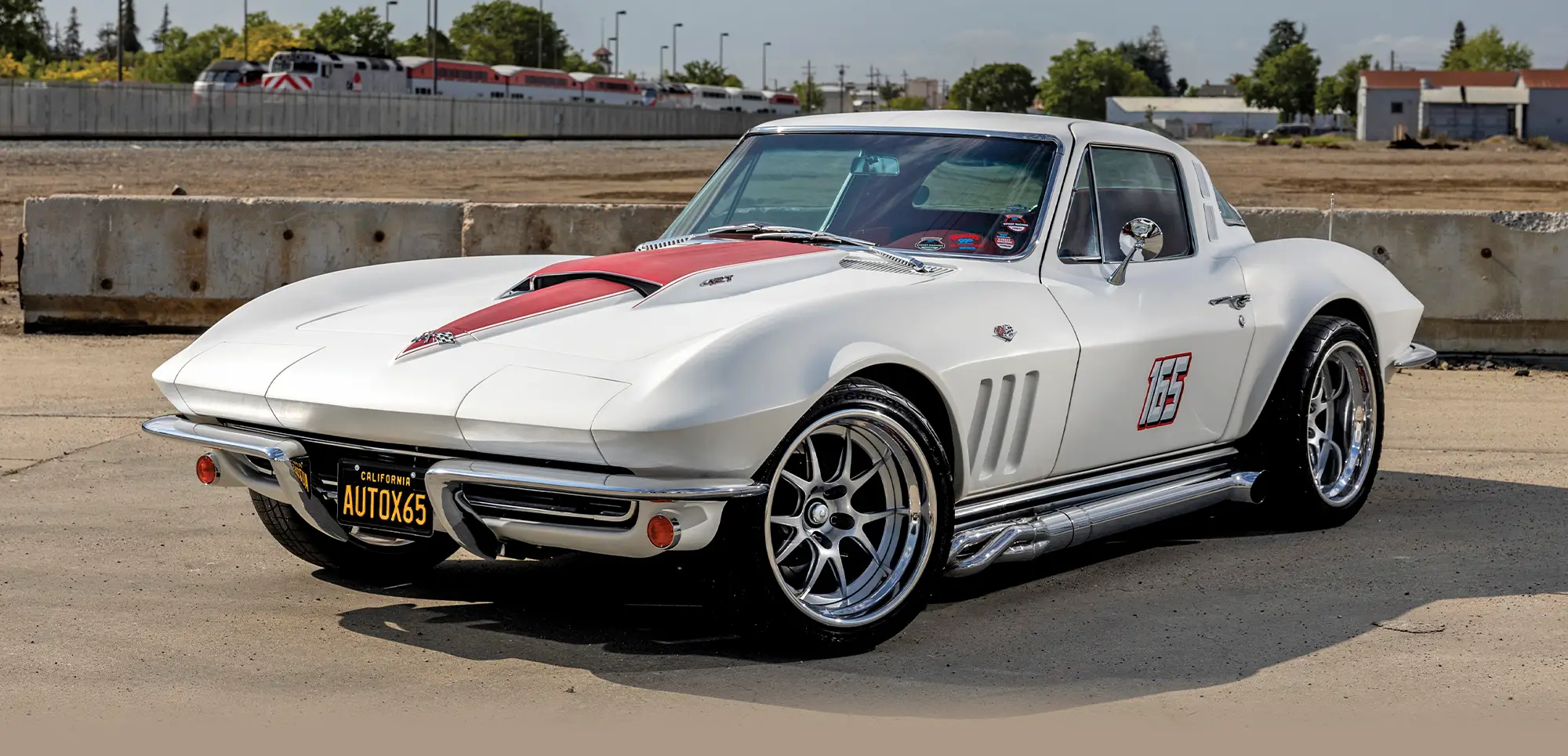Custom white 1965 Chevrolet Corvette with a red hood stripe, chrome side pipes, and modern custom alloy wheels.