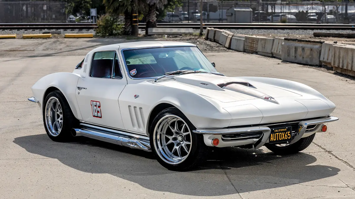 Custom white 1965 Chevrolet Corvette front three-quarter view, showing the red hood stripe, chrome side exhaust, and custom alloy wheels.