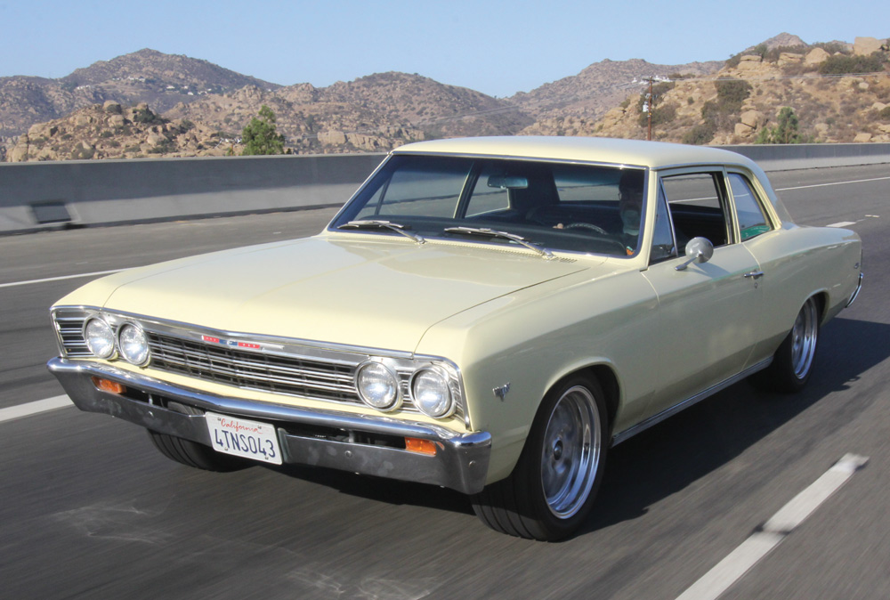 A classic, light-yellow 1966 Chevrolet Chevelle 300 sedan is pictured driving on a California freeway. The car has aftermarket wheels and a lowered stance, suggesting performance modifications.