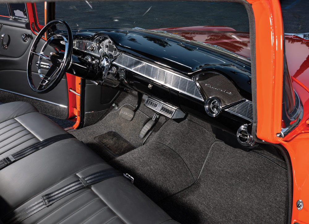Interior shot of the classic Chevy 210's cabin, highlighting the black leather upholstery, dark gray carpet, polished black dashboard, and modern chrome accents.