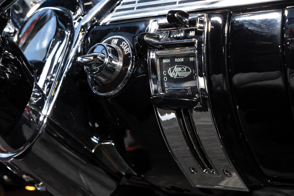 Close-up of the polished black dashboard showing the ignition key barrel and a chrome-accented lever for the classic-style climate control/heater system.