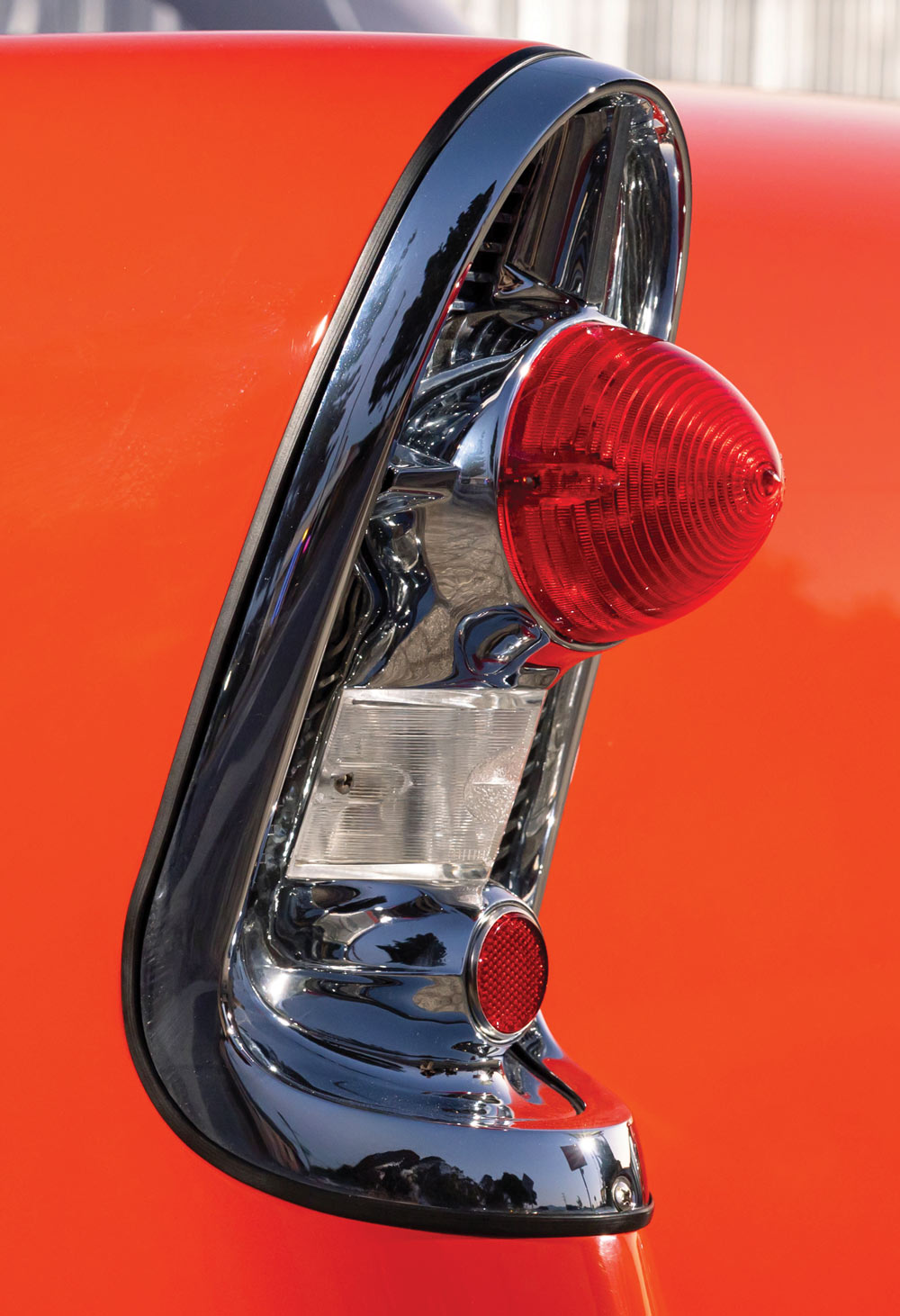 A close-up detail of the custom tail light on the orange 1956 Chevrolet 210 sedan, featuring a prominent red lens enclosed by a vertical chrome trim piece.