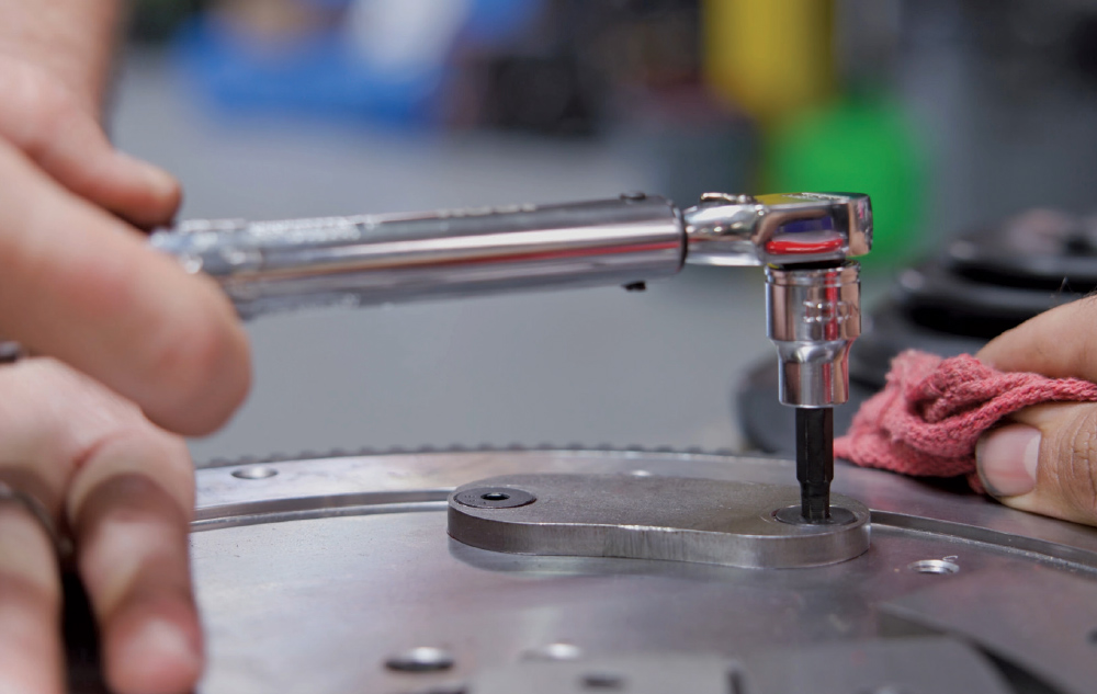 Close-up of hands using a torque wrench with an Allen bit to tighten a bolt on a clean, metallic flywheel assembly.