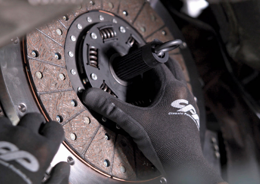A mechanic's gloved hands inserting a clutch alignment tool into the center of a newly installed clutch disc assembly.