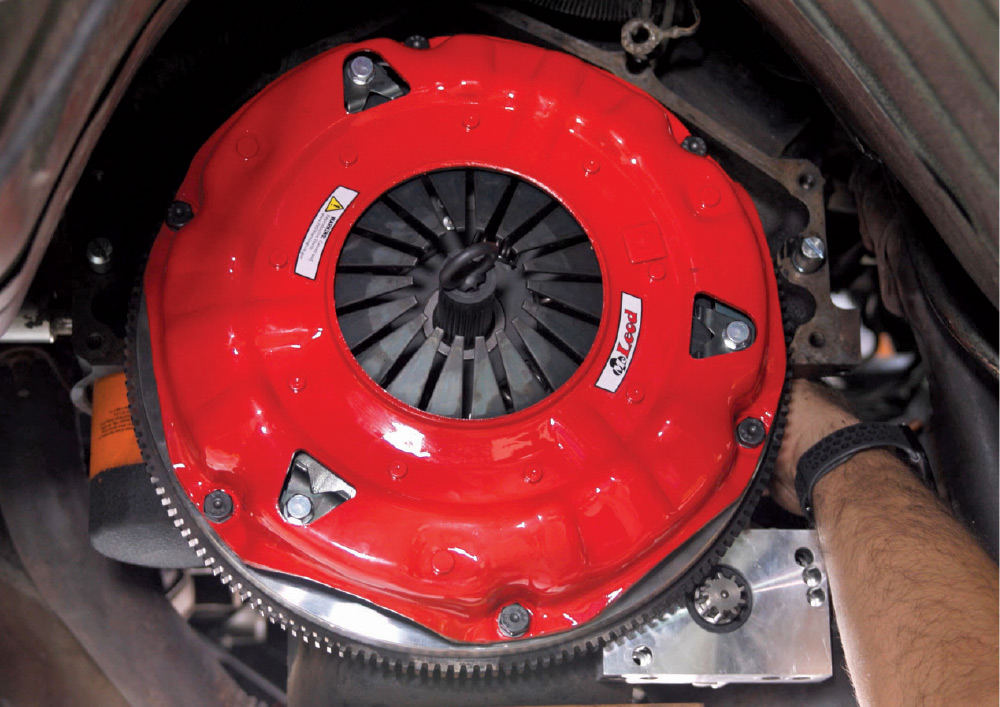 Close-up view from beneath a car of a bright red clutch pressure plate bolted to the flywheel, ready for the transmission installation.