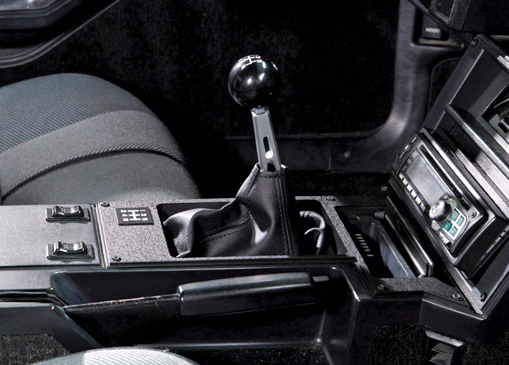 Close-up of a car's interior showing a new manual shifter with a black ball knob and leather boot installed in the center console next to the handbrake and radio.