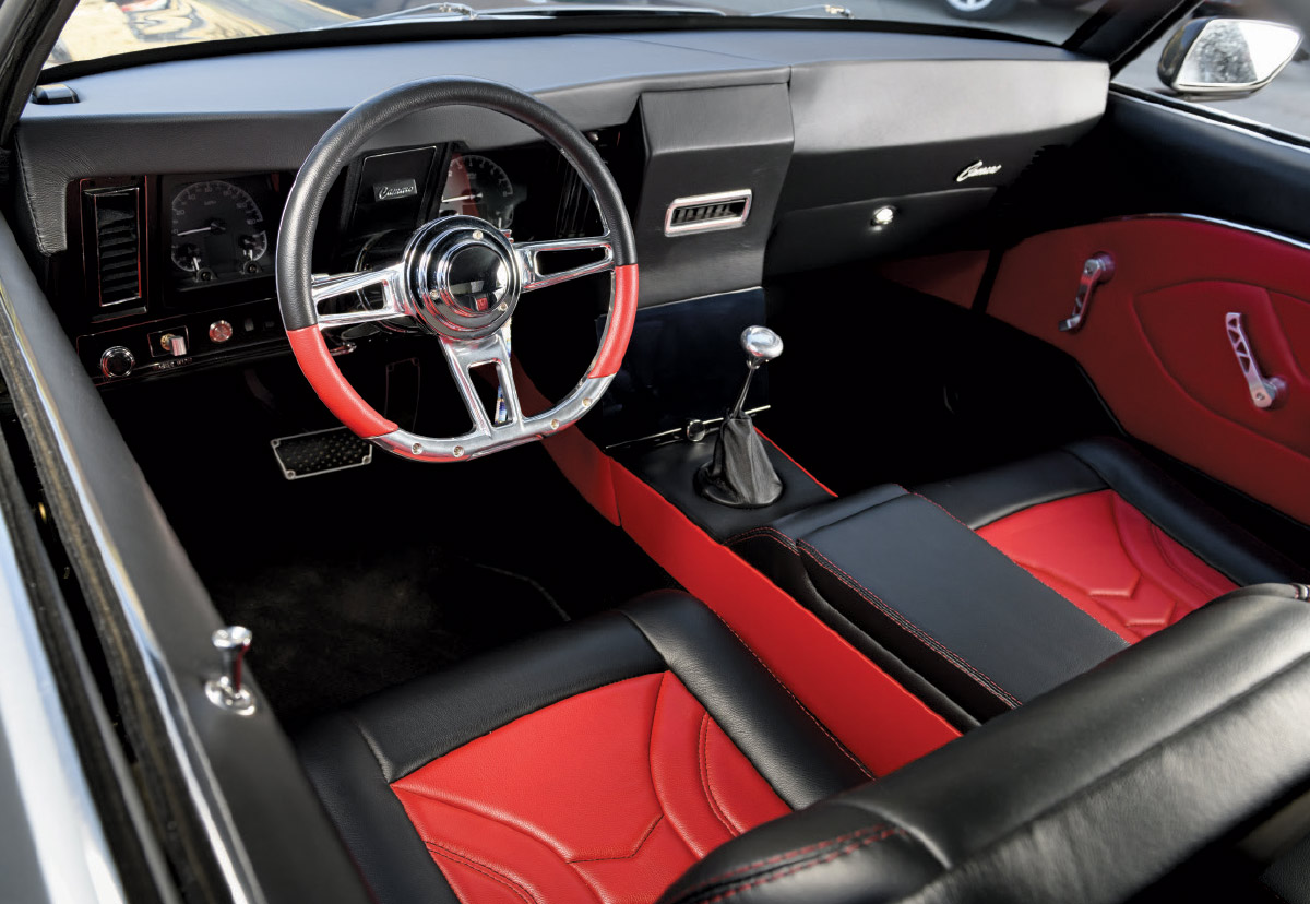 Interior view of a custom 1969 Camaro with black and red leather seats, a custom black dashboard, and a chrome steering wheel with red accents.
