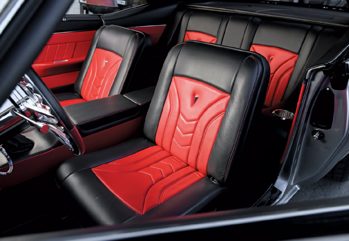 Close-up of the front and rear seats of a custom Camaro interior, featuring black and red leather upholstery with matching stitching and center console.