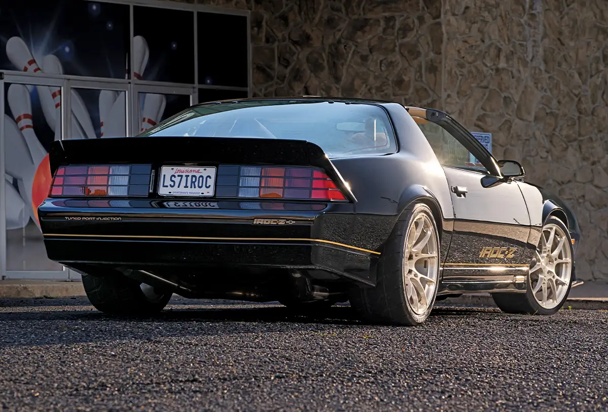 A modified third-generation Camaro Z28 featuring custom gold "IROC-Z" decals, a tan integrated roll cage, and a high-performance exhaust system.