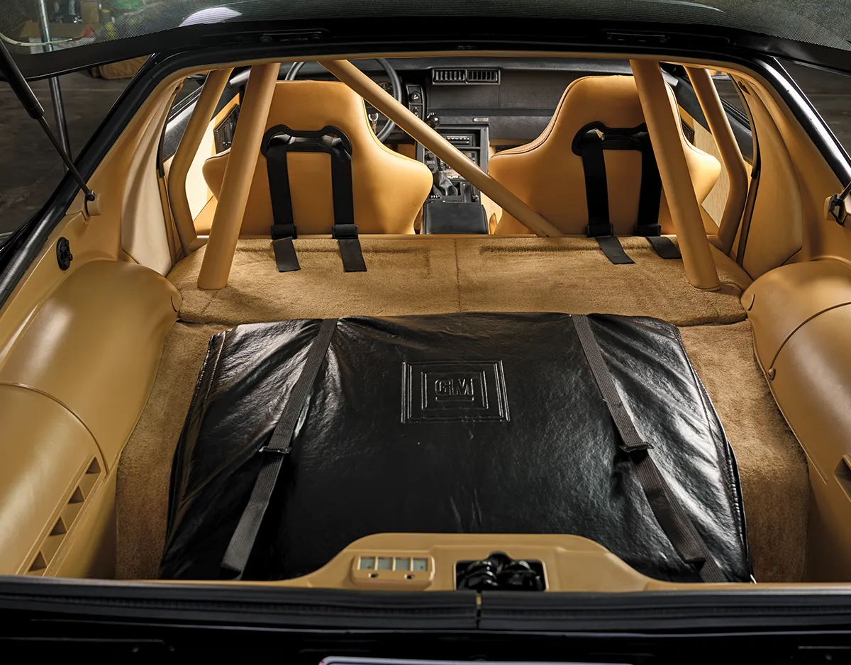 A meticulously restored Camaro Z28 interior with tan upholstery, high-back bucket seats with racing harnesses, and a custom-fitted roll bar system.