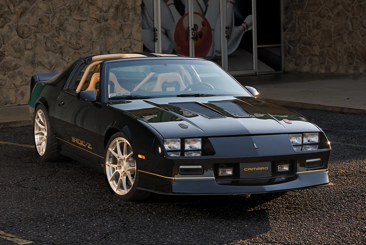 Front three-quarter view of a custom black Chevrolet Camaro IROC-Z featuring gold BC Forged wheels and a tan roll cage.