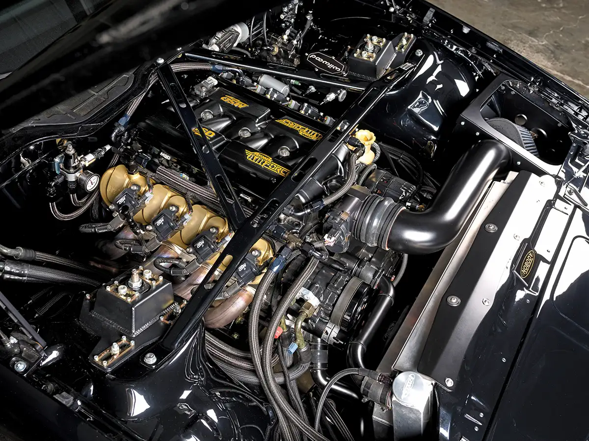High-performance car engine bay with a clean black finish, upgraded cooling system, Wilwood master cylinder, and reinforced strut tower bracing.