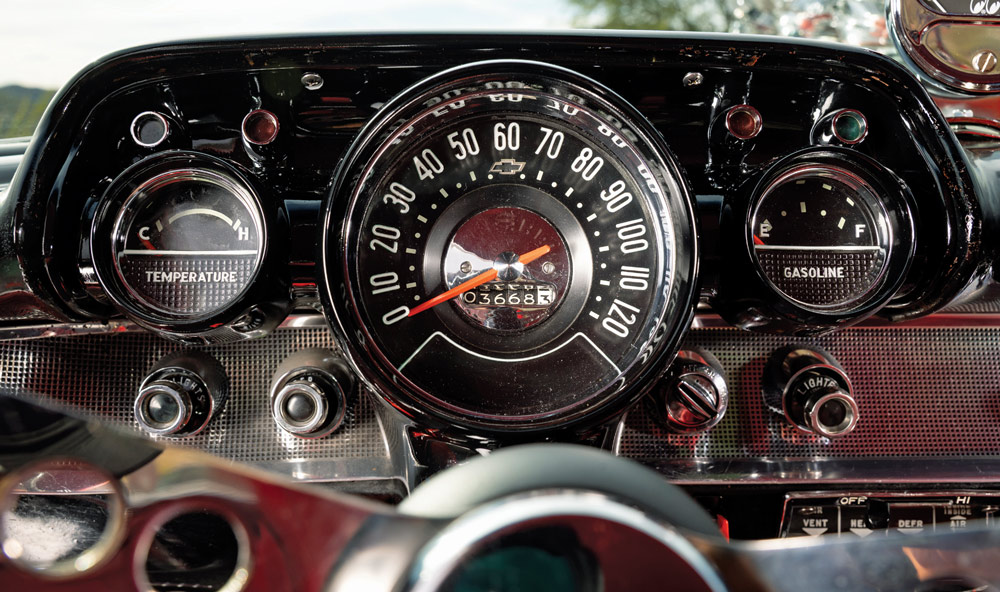 Close-up of a classic 1957 Chevrolet dashboard featuring a central 120-mph speedometer, temperature and fuel gauges, and vintage-style chrome control knobs and switches.