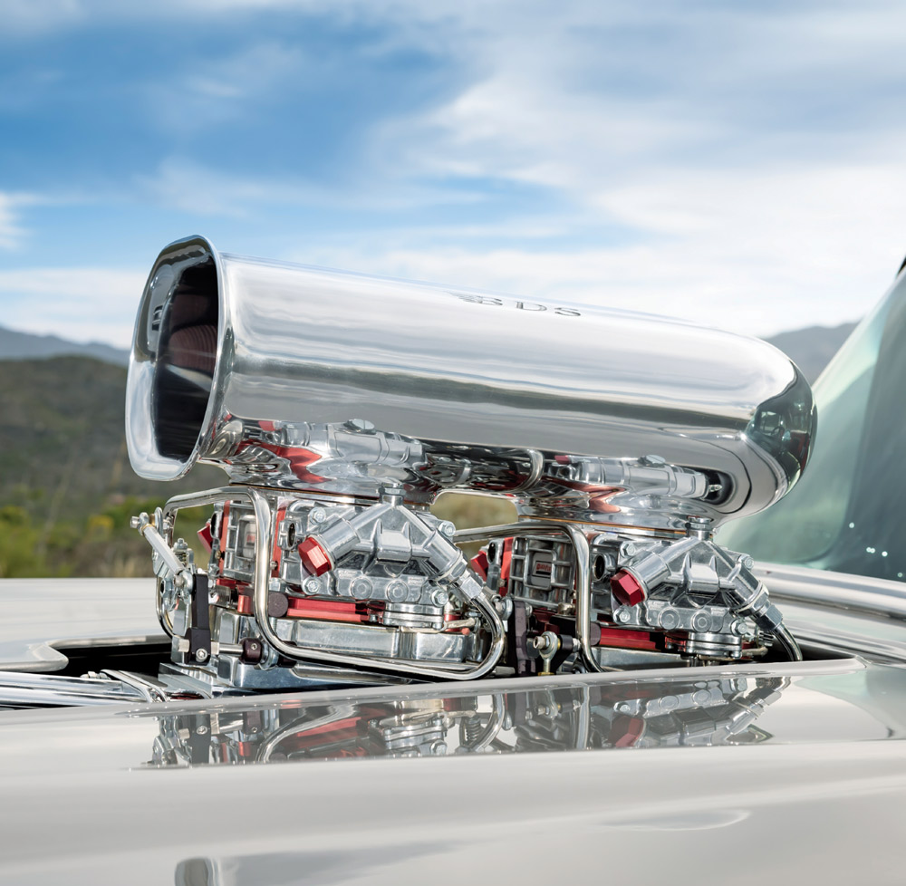 Detailed side view of a polished BDS air scoop and dual-quad carburetor setup protruding through a custom cutout in the silver hood of a high-performance drag car.
