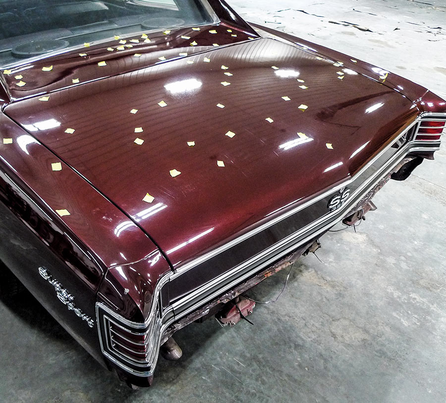 High-angle view of a classic maroon Chevrolet Chevelle SS trunk with yellow tape markers for hail damage repair.