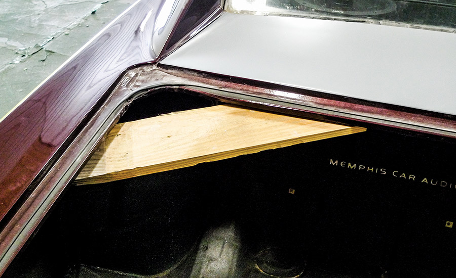 Interior view of a classic car trunk with a custom Memphis Car Audio setup being braced for auto body repair work.