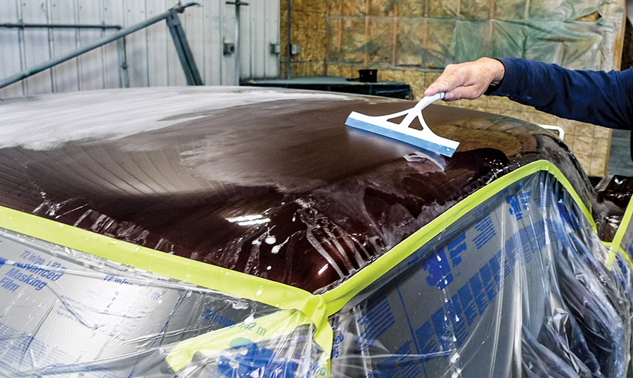Close-up of wet-sanding prep on a vintage muscle car roof, featuring protective 3M masking film and a squeegee to clear residue for a smooth paint finish.