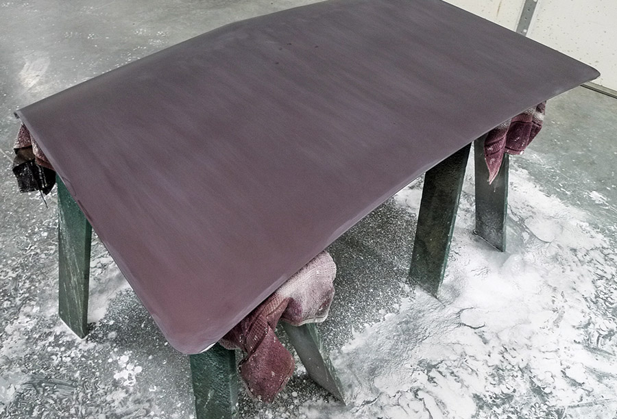 Detached classic car roof panel resting on sawhorses during the final wet-sanding stage of a maroon Chevrolet Chevelle restoration.